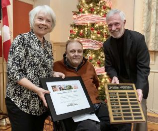 Neil Allan, (middle) chair of the Frontenac Accessibility Advisory Committee, presenting the 2019 Accessibility Award to Susan Ward-Moser, chair of the board for Southern Frontenac Community Services, while Warden Ron Higgins (left) holds up the plaque listing all of the previous award winnners, at the Frontenac County Warden's reception which was held at the Grace Centre last Thursday (December 12)